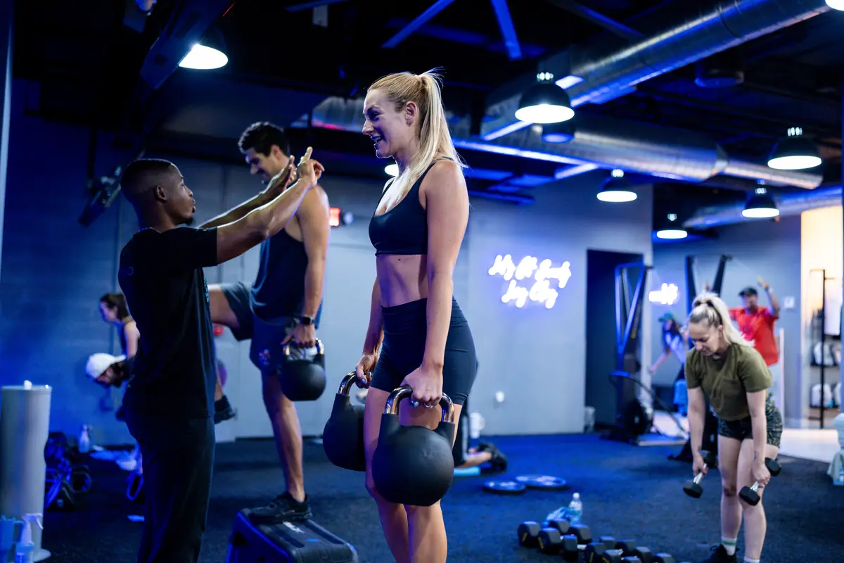 SWEAT440 coach giving form cues to members lifting kettlebells