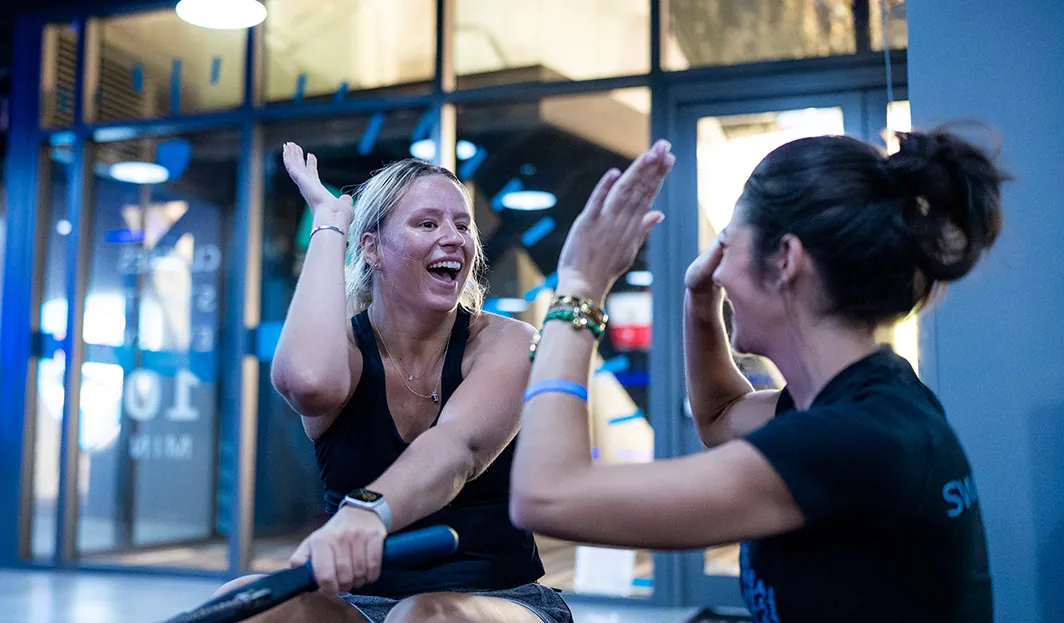 SWEAT440 member on a rower high-fiving a coach inside a SWEAT440 franchise studio